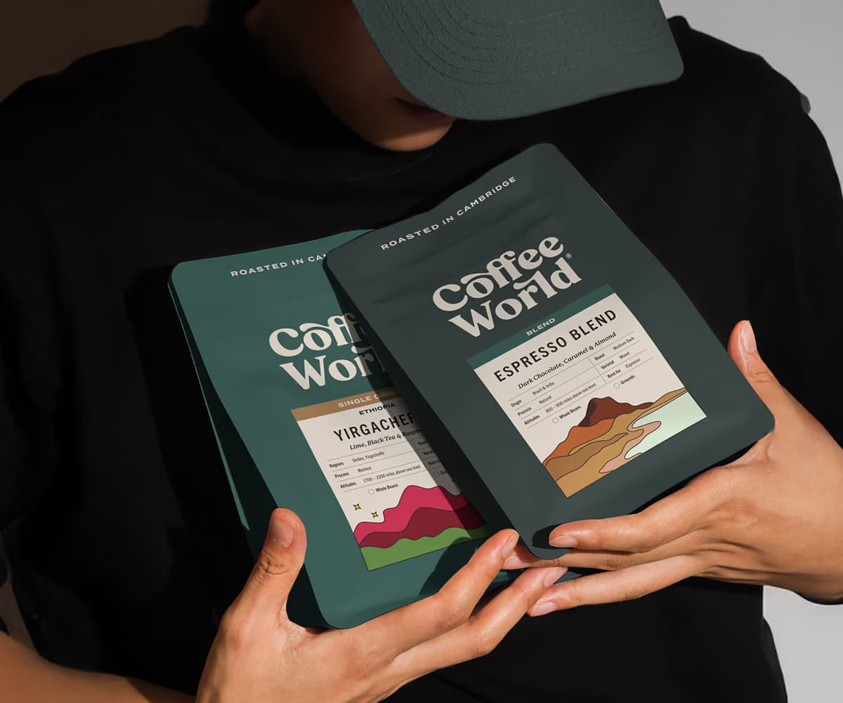 Two Coffee World packaging bags held by hands, showing the rebranded dark slate-green design — Coffee World UK identity study case by SCANR and Widarto Impact.