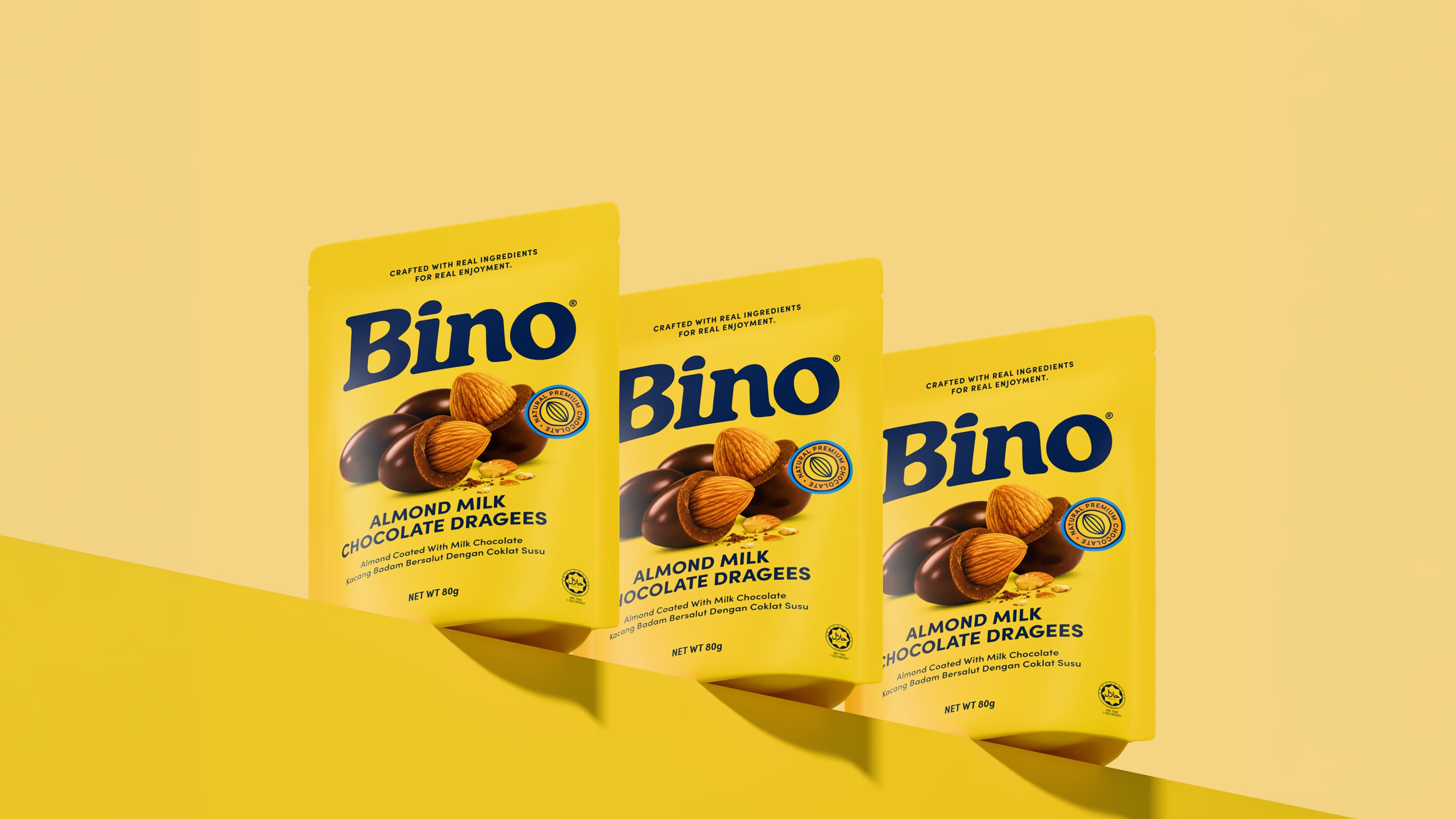 Three yellow packs of BINO Almond Milk Chocolate Dragees arranged against a yellow background.